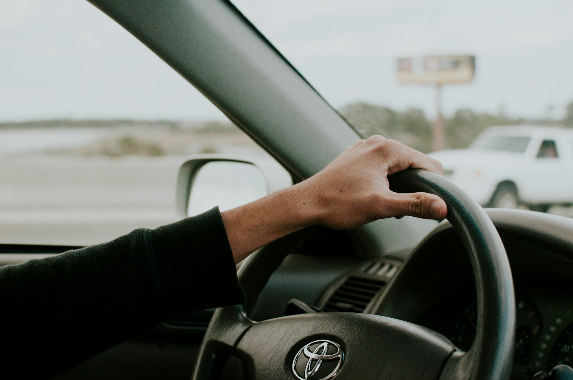Close-up van een hand op het stuur van een Toyota tijdens het rijden op een rustige weg
